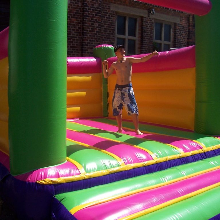 Hüpfburg Verleih, Hüpfburgen Vermietung Leipzig Wahren Junger Mann springt fröhlich in einer bunten Hüpfburg mit Pink- und Grüntönen. Leipzig Wahren